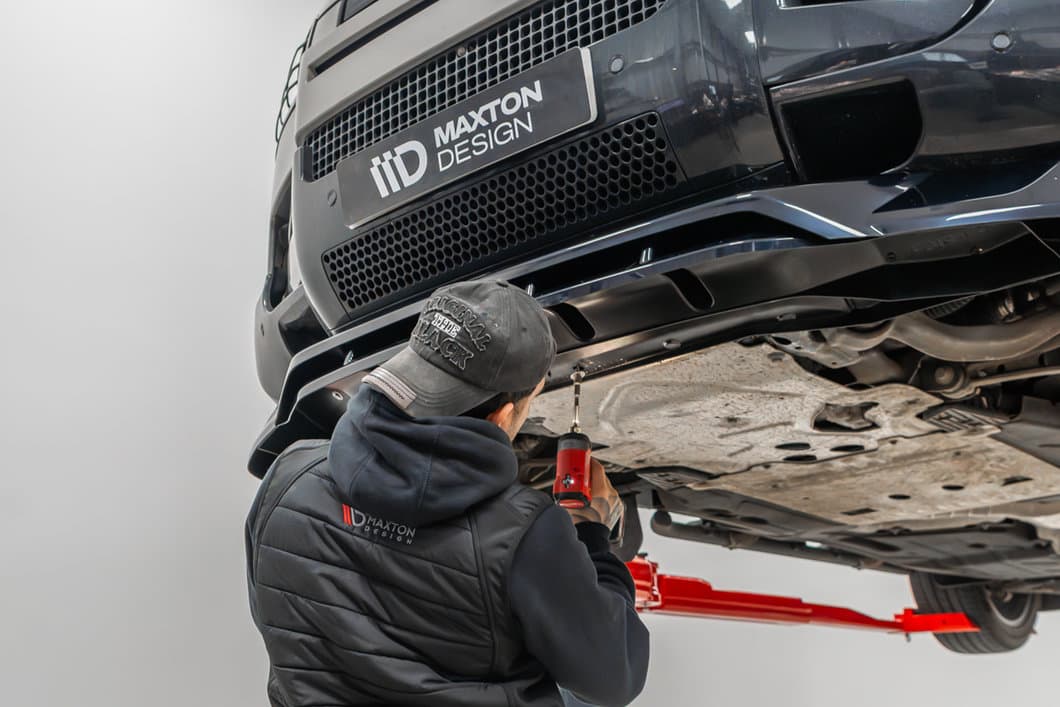 Maxton Design technician securing a front splitter with a screwdriver under a car on a lift